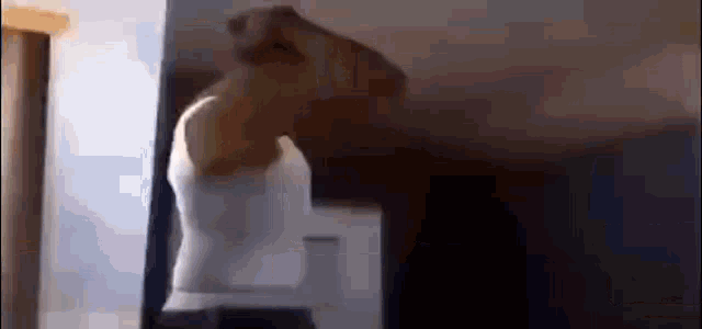 a man in a white tank top is standing in front of a mirror in a dark room .