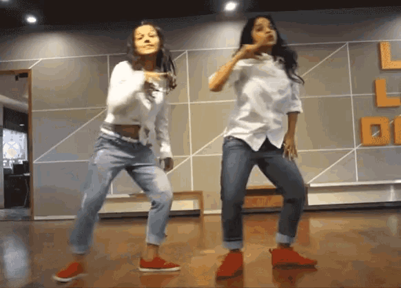 two women are dancing in front of a wall that has the letter l on it .