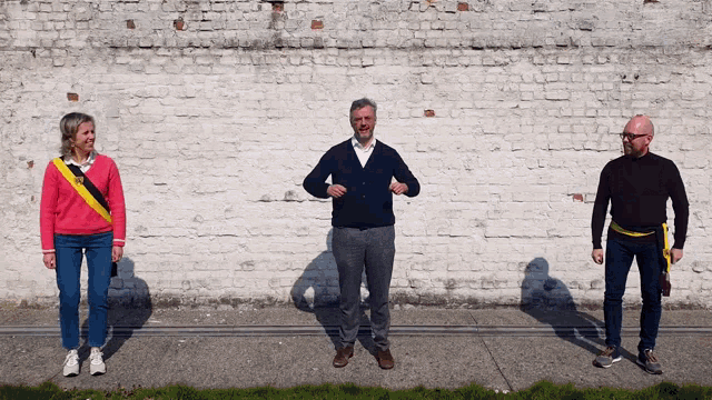 three people stand in front of a brick wall