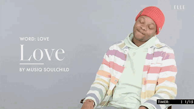 a man wearing a rainbow colored jacket is sitting in front of a sign that says " love "