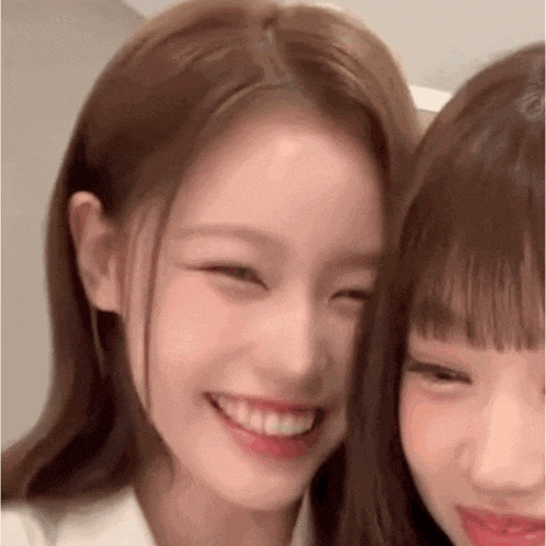 two girls are smiling for the camera and looking at the camera .