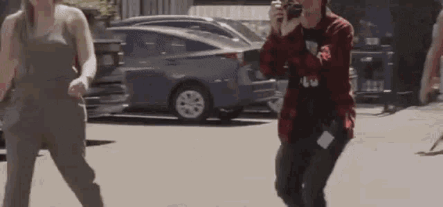 a man is taking a picture of a woman dancing on the street while a woman looks on .