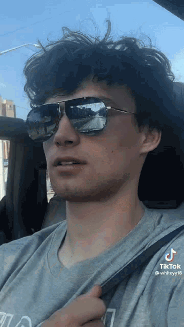 a man wearing sunglasses is sitting in a car with his seat belt on .