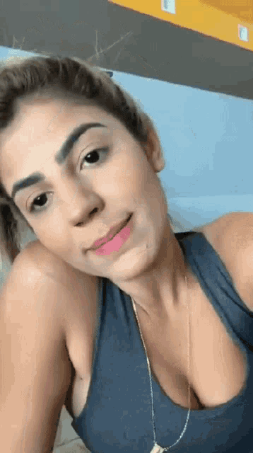 a woman wearing a blue tank top and a necklace is looking at the camera .