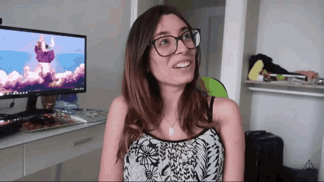 a woman wearing glasses smiles in front of a computer screen