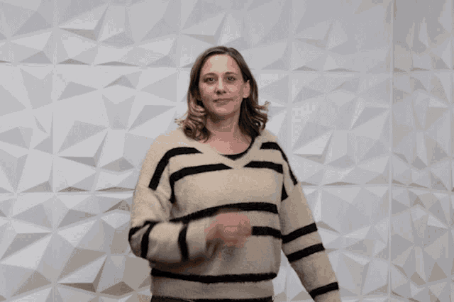 a woman in a striped sweater stands in front of a white wall and says thank you