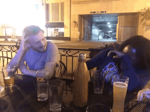 a man sits at a table with two glasses of beer and a bottle of beer with the letter x on it