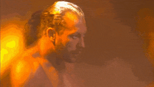a man with long hair and a ponytail looks at the camera in a dark room