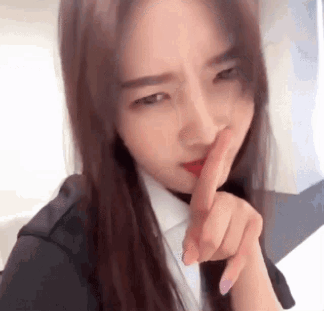 a young woman is making a shhh gesture with her finger to her mouth .
