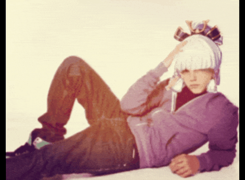 a man wearing a purple hoodie and a white hat is laying on the floor