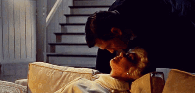 a man kisses a woman laying on a couch in front of stairs