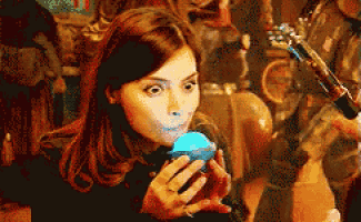 a woman is holding a blue ball in her hands and blowing it out of her mouth .