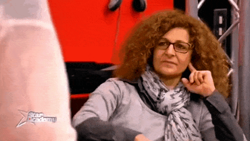 a woman with curly hair and glasses is sitting in front of a red wall and talking on a cell phone .