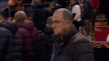 a man in a jacket is standing on a soccer field with a crowd in the background .
