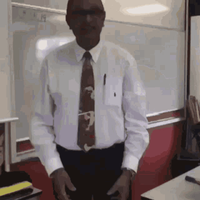 a man in a white shirt and tie stands in a classroom