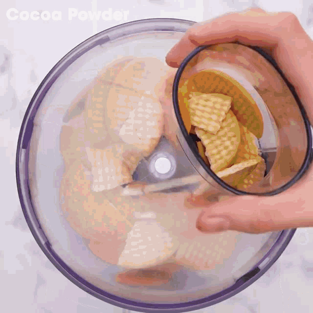 cocoa powder is being poured into a food processor filled with cookies