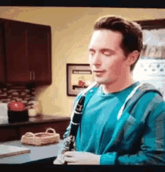 a man in a blue shirt playing a clarinet in a kitchen