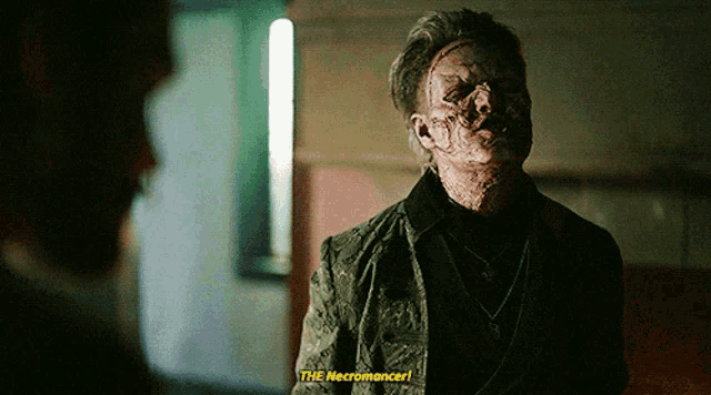 a man with blood on his face is talking to another man and says " the necromancer " in yellow letters