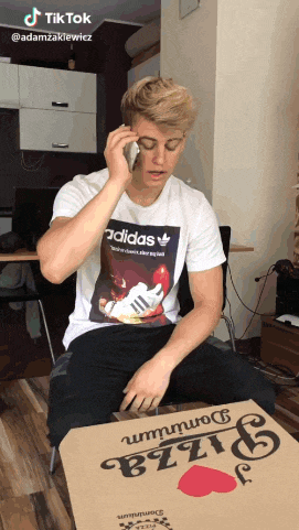 a man wearing an adidas t-shirt is talking on a cell phone