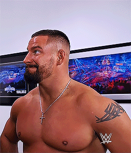 a shirtless man with a beard and a cross necklace is standing in front of a wall with pictures .