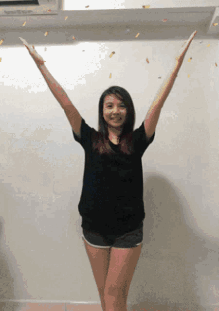 a woman in a black shirt and shorts is standing with her arms outstretched and confetti falling around her