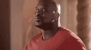 a man in a red shirt is standing in front of a mirror and looking at the camera .