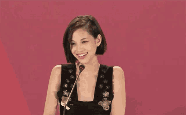 a woman in a black dress stands in front of a microphone