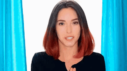 a woman with red hair is standing in front of a blue curtain and making a funny face .