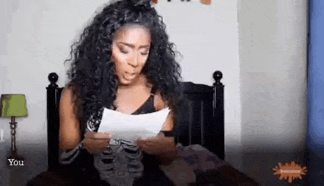 a woman is sitting on a bed holding a piece of paper in her hands .