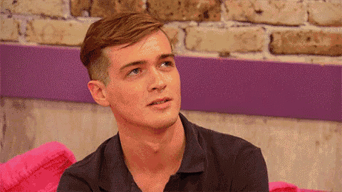 a young man is sitting on a pink couch in front of a brick wall looking up .