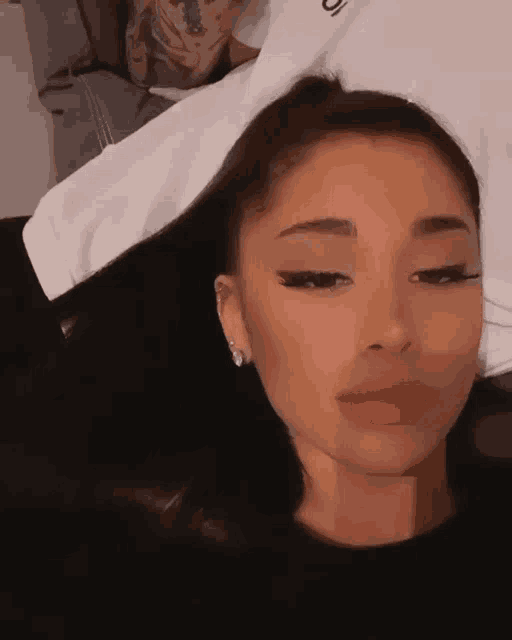 ariana grande is wearing a black shirt and earrings and making a face .