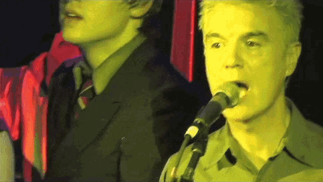 a man singing into a microphone with another man in the background