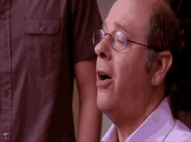 a bald man wearing glasses and a purple shirt is making a surprised face .