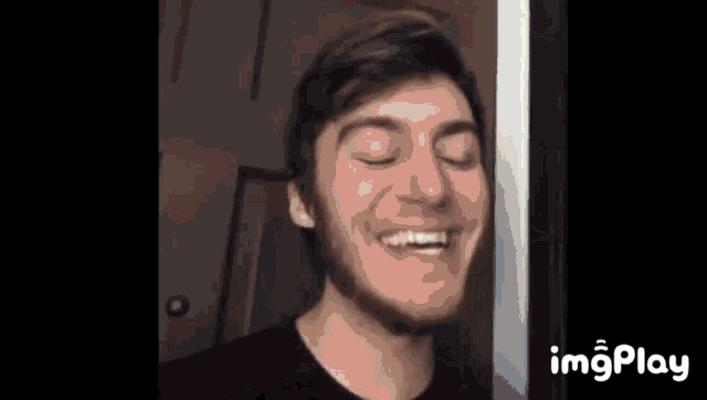 a young man with a beard is smiling with his eyes closed and his mouth open .