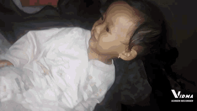 a baby laying on a bed next to a screen recorder logo