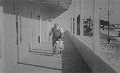 a man and a woman are standing on a balcony looking out a window .