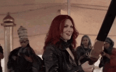 a woman with red hair is holding a large sword in front of a crowd .