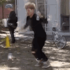 a man in a black shirt is jumping in the air while a bicycle is parked in the background .