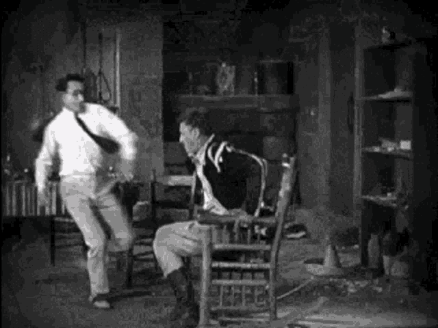 a man is sitting in a rocking chair while another man is dancing in a room .