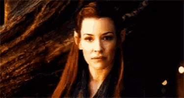 a woman with red hair and elf ears is standing in front of a tree .