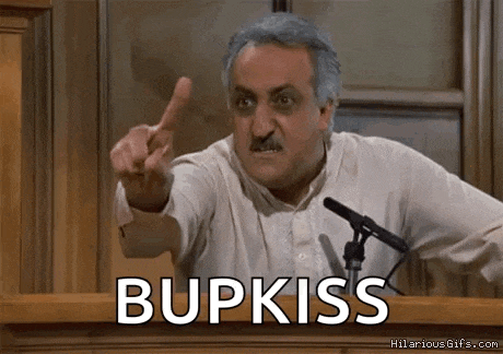 a man is giving a speech in front of a microphone and pointing at the audience while saying bupkiss .