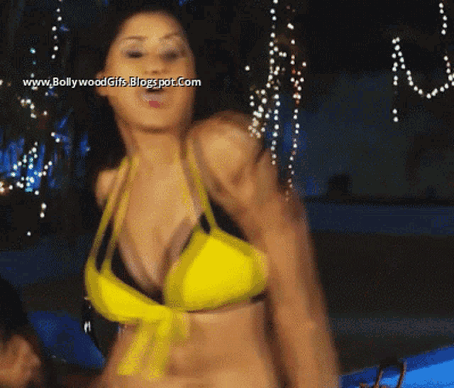 a woman in a yellow bikini is dancing in front of a sign that says www.bollywoodgifs.blogspot.com on it