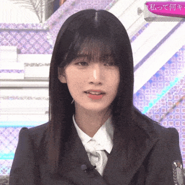 a woman in a suit and tie stands in front of a sign that says 私 って 何 キ
