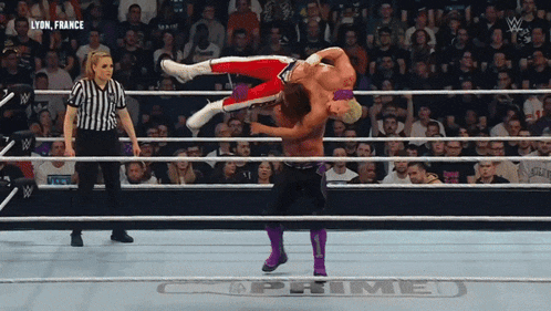 a wrestler in a purple outfit is doing a flip over another wrestler in a ring that says prime