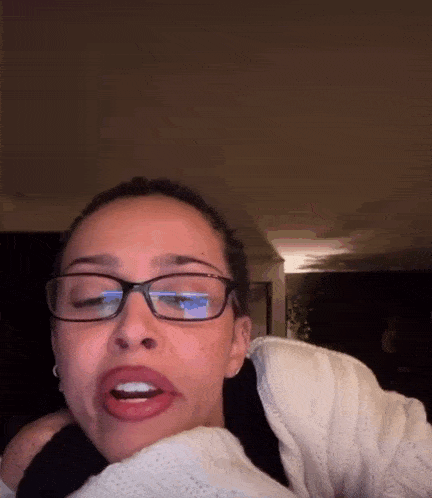 a woman wearing glasses and a white sweater with her mouth open