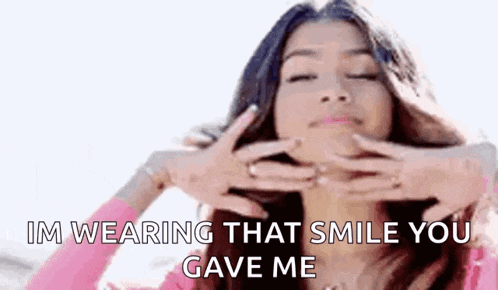 a woman is wearing a pink shirt and making a face with her hands and says `` im wearing that smile you gave me '' .