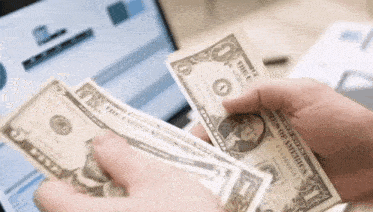 a person is counting money in front of a laptop computer .