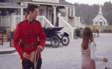 a man in a red uniform is holding a hat and talking to a girl in front of a church .