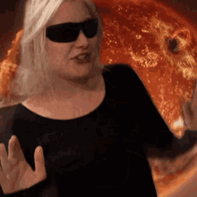 a woman wearing sunglasses and a black shirt stands in front of a pizza