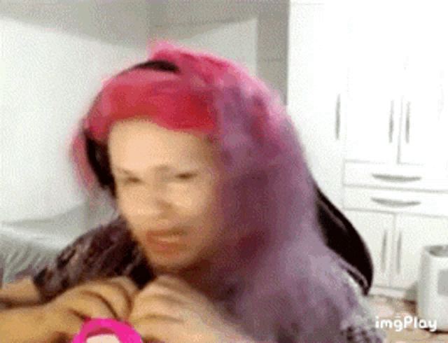 a woman with pink hair is making a funny face while holding a pink object .